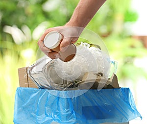 Man putting used paper cup into trash bin on blurred background. Recycling problem