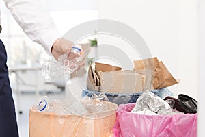 Man putting used plastic bottle into trash bin in office. Waste recycling