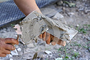 Man putting wet paste cement mortar mix on masonry trowel with metal spattle, one hand blurred to emphasise action, closeup detail