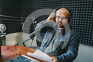 Man radio host or representer or journalist reads news from paper list in hand to studio microphone sitting at mixing sound panel photo