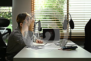 Man radio host wearing headphone and talking through microphone recording podcast in small home studio