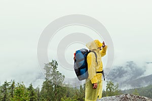 Man in a raincoat with a backpack on his back stands on a rock and looks away at the beautiful views and looks away