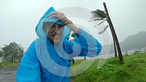 A man in a raincoat is under a hevy rain and stormy wind. Shot on an action camera. Tropical storm concept. Contains