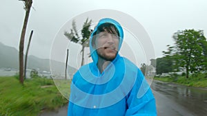 A man in a raincoat is under a hevy rain and stormy wind. Shot on an action camera. Tropical storm concept. Contains