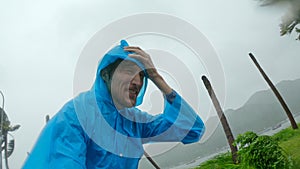 A man in a raincoat is under a hevy rain and stormy wind. Shot on an action camera. Tropical storm concept. Contains