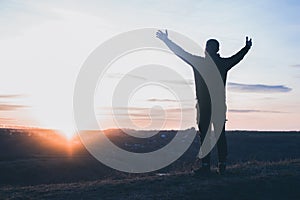 A man with raised hands is praying. On the background of the sunset sky. Repentance for sins. Kneeling Prayer to God. Worship