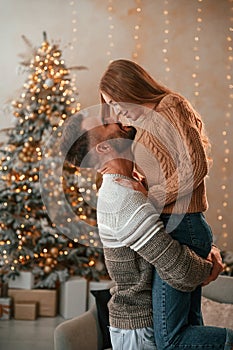 Man raised and holds the woman in his hands. Lovely young couple are celebrating New Year at home