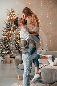 Man raised and holds the woman in his hands. Lovely young couple are celebrating New Year at home