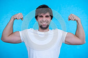 Man raises arms and shows biceps demonstrates muscles feels proud about personal achievements on a blue background