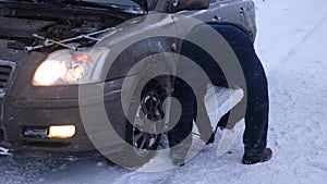 Man raises car jack on road. man is changing wheel of car. replacement wheels in winter on road in a blizzard and