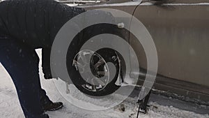 Man raises car jack on road. man is changing wheel of car. replacement wheels in winter on road in a blizzard and