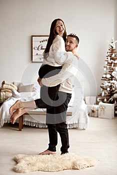 Man raises his wife standing in a bright room with bright and stylish Christmas decor