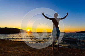 Man raising hands at sunset on the beach