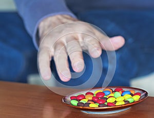 A Man Reaches for Colored Candies in a Dish