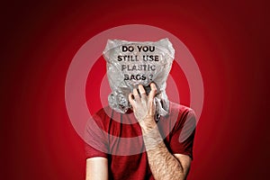 The man reaches for his mouth, feeling suffocated in a plastic bag. Red background. Concept of pollution and