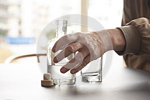 Man reaches out for a bottle of alcohol and an empty glass by the side at a table in home or bar environment. Selective focus on h