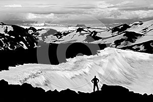 Man reaching mountain summit, watching glaciers and snowfields in Iceland.