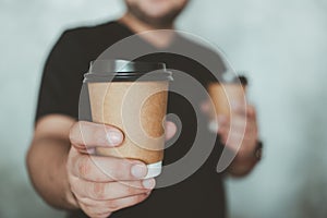 Man reaching out a brown hot coffee cup of coffee giving you. Male bringing coffee