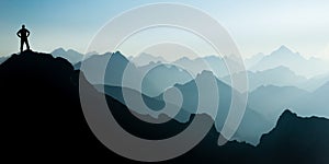 Man reaching summit after climbing and hiking enjoying freedom and looking towards mountains silhouettes panorama during