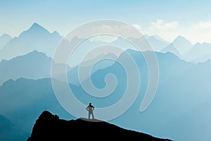 Man reaching summit after climbing and hiking enjoying freedom and looking towards mountains silhouettes panorama during