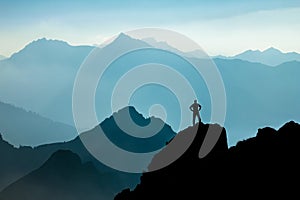 Man reaching summit after climbing and hiking enjoying freedom and looking towards mountains silhouettes panorama during