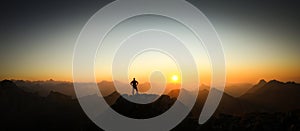 Man reaching summit enjoying freedom and looking towards mountains sunrise.