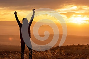 Man reaching summit enjoying freedom and looking towards mountains sunset.