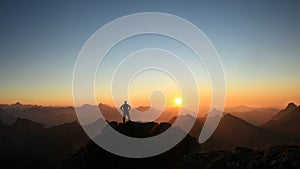 Man reaching summit enjoying freedom and looking towards mountains sunset.