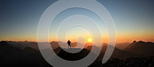 Man reaching summit enjoying freedom and looking towards mountains sunset.