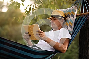 Man reading book in comfortable hammock at green garden