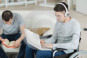 Man reading book disabled friend using laptop