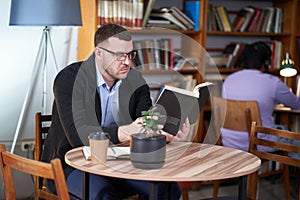 Man reading book and drinking coffee in a cafe with many books on a background