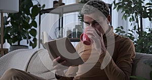 Man reading a book and drinking coffee on sofa at home