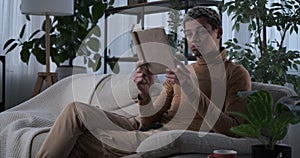 Man reading a book and drinking coffee on sofa at home