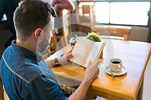 Man Reading Book And Enjoying Coffee At Cafe