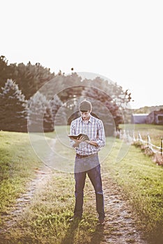 Man reading a book in a garden surrounded by greenery under sunlight with a blurry background