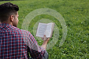 Man reading book on green grass, back view