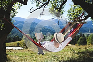 Man reading book in hammock outdoors on sunny day