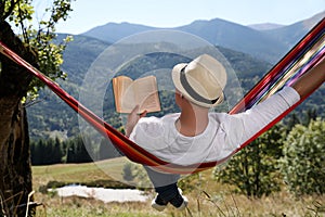 Man reading book in hammock outdoors on sunny day