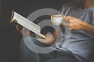 A man reading a book and holding cup of coffee.