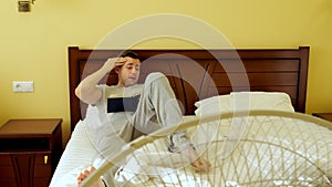 A man is reading a book lying in bed. Summer heat. The fan works.