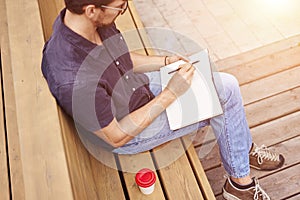 Man reading book sitting outside in public space. Wearing glasses alone working. Concept of education or busyness