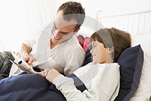 Man reading book to young boy in bed smiling