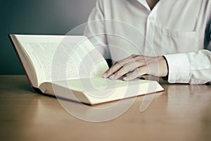 A man reading a book on wooden table with vintage filter blurred background