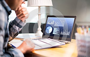 Man reading business report paper. Laptop with financial graphs