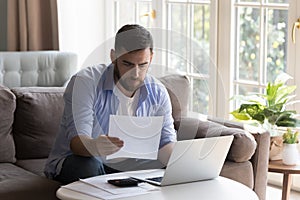 Man reading documents, examining bills doing paperwork at home