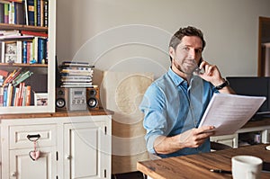 Man reading documents and talking on a cellphone at home