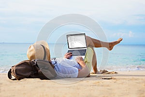 Man reading email on laptop while relaxing on beach photo