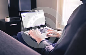 Man reading email and using laptop in home living room. Checking received electronic web mail and replying to messages.