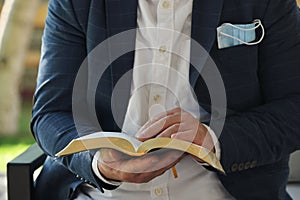 Man Reading Holy Bible with a medical mask sticks out of a pocket